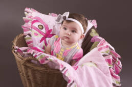 Portrait photograph of baby sitting in basket with pink blanket
