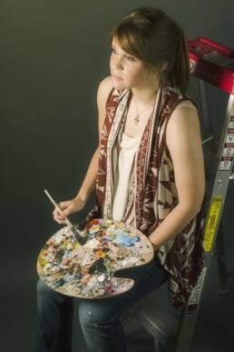 Portrait of girl sitting on ladder with paint and paint brush