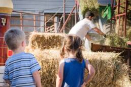 Photograph of two children watching farmhand throwing hay