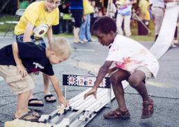 Event photograph of children playing with pinewood derby cars on track