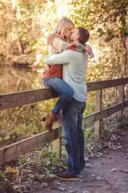 Engagement photograph of couple kissing while girl sitting on fence